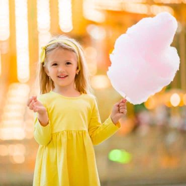 Jeune fille devant un carrousel avec une barbe à papa